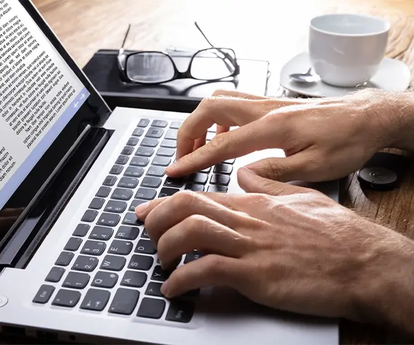 Personne utilisant un ordinateur portable sur un bureau avec une tasse de café, accompagné d’un encart présentant un cabinet de formation tunisien spécialisé en gouvernance et sécurité des systèmes d’information, avec 10 ans d’expérience.